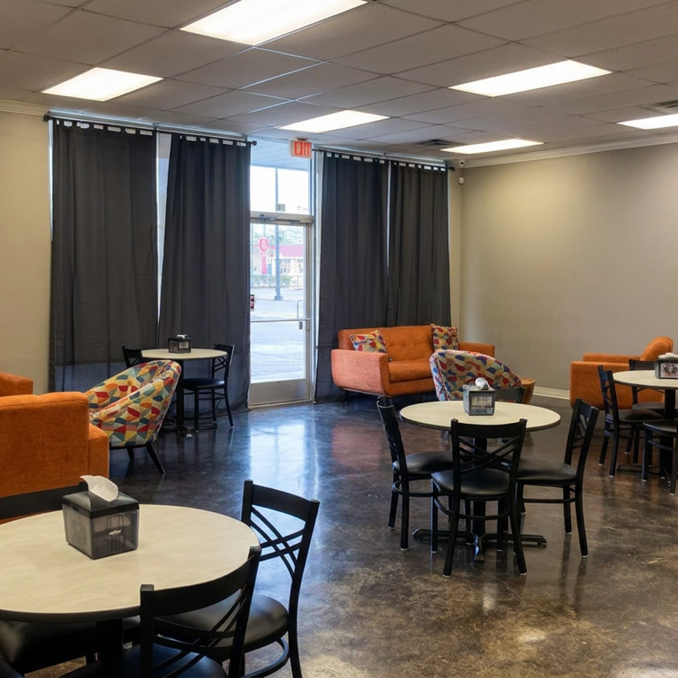 Spacious restaurant lounge with orange sofas, patterned armchairs, round tables, black chairs, and a polished concrete floor.