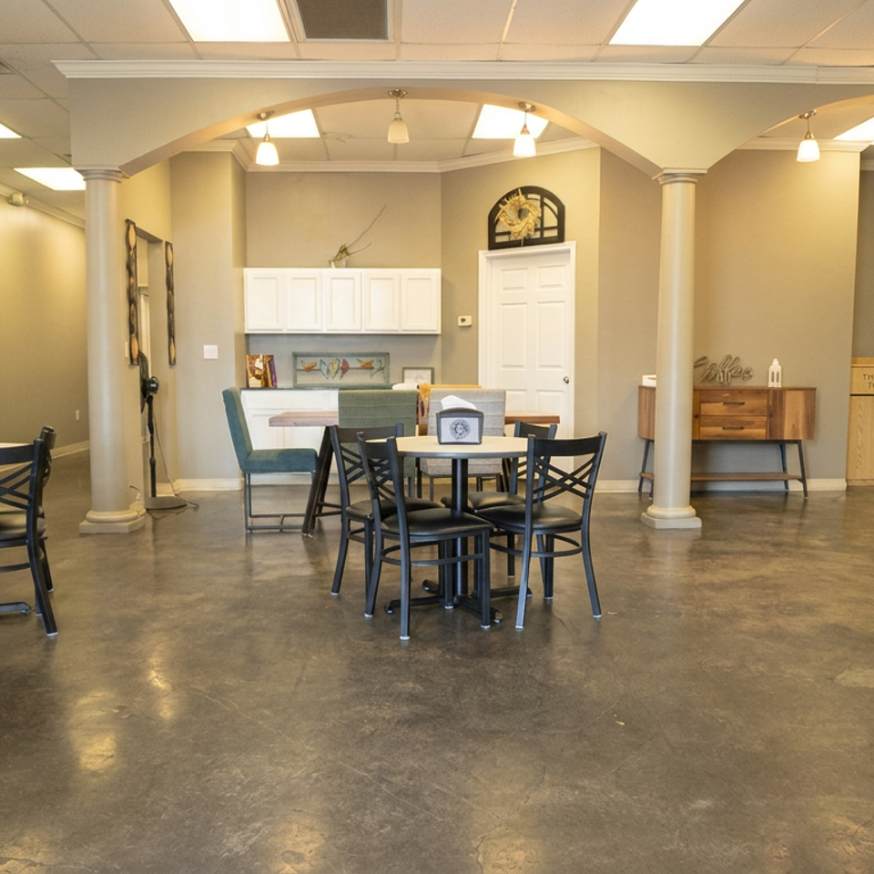 Spacious restaurant dining room with black tables, chairs, polished concrete floors, decorative columns, and a cozy seating area.